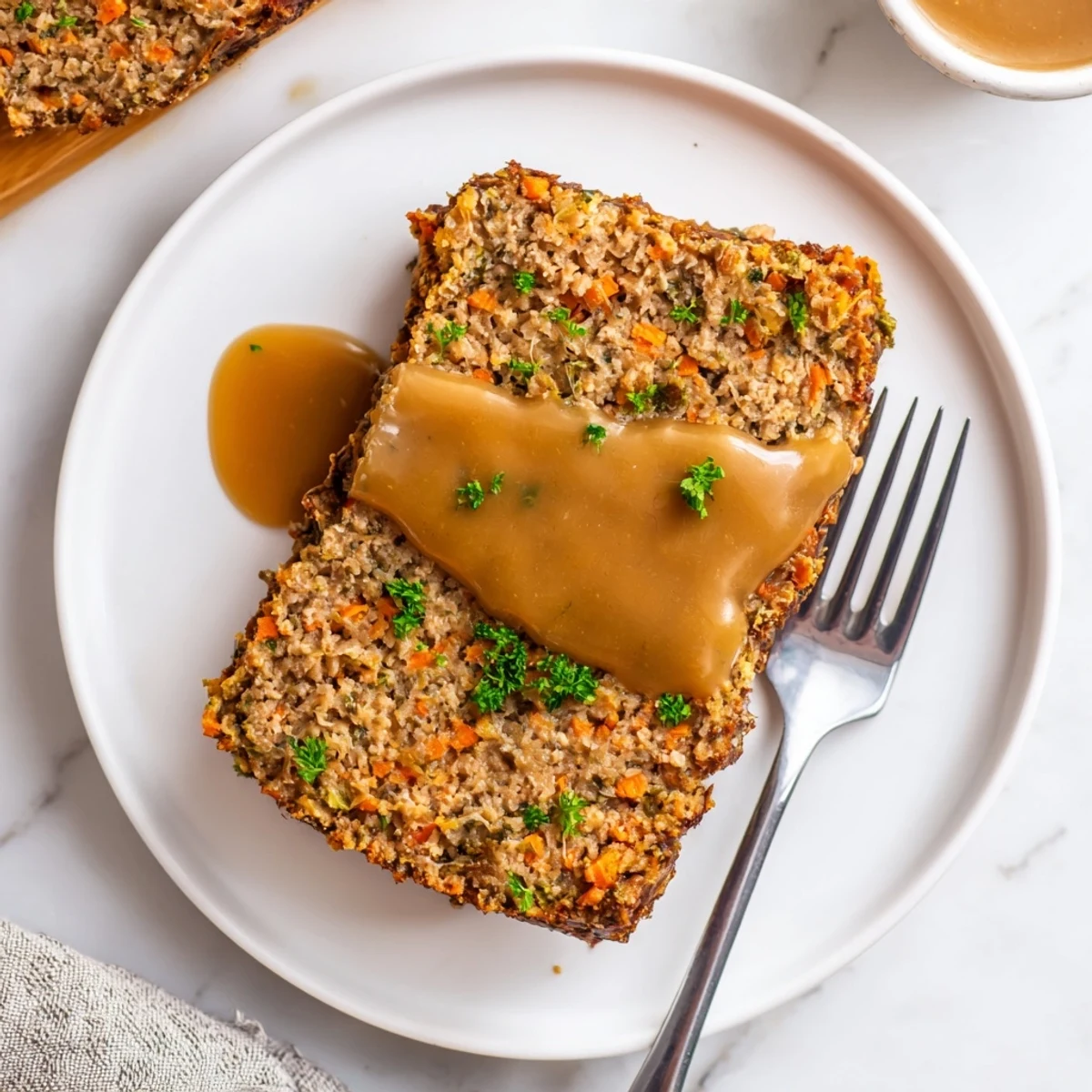 Würziges Turkey Loaf Slice mit hausgemachter Grafe auf weißem Teller, serviert über nussigen Kartoffelpüree und grünen Erbsen, ideal für ein herzhaftes Familienessen.