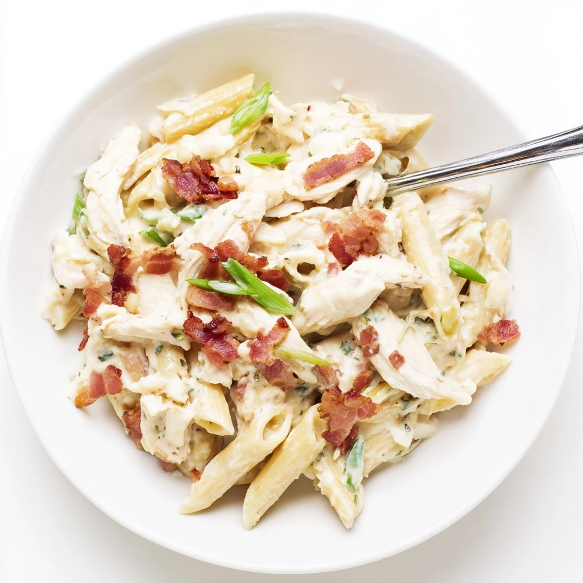 Cremiges Crack Chicken Pasta mit knusprigem Bacon und geriebenem Cheddar auf einem weißen Teller