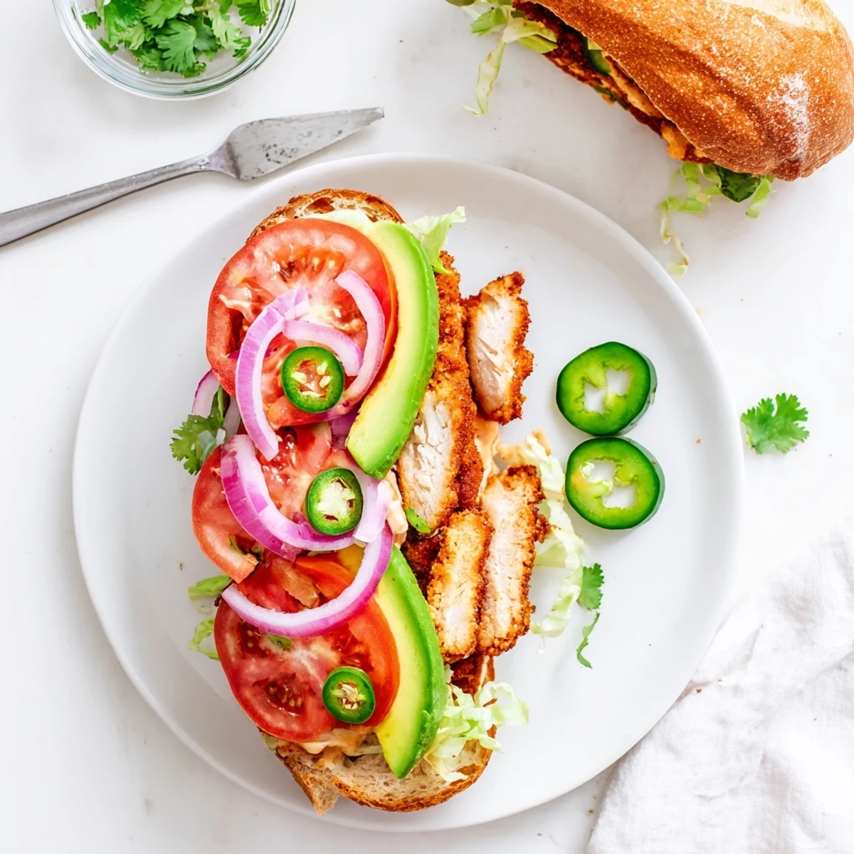 Mouthwatering chicken torta sandwich stacked with sliced avocado, tomatoes, and jalapeños on bolillo roll
