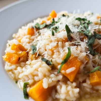 A bowl of Winter Squash Risotto with Sage and Parmesan next to a glass of white wine on a table