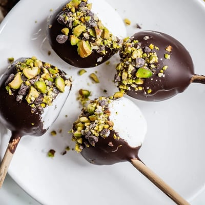 Chocolate Dipped Marshmallows arranged on parchment paper, some rolled in crushed nuts and others in shredded coconut.