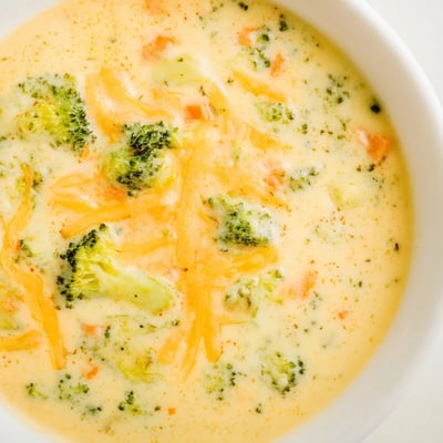 Golden bowl of homemade Instant Pot Broccoli Cheddar Soup with broccoli florets and grated carrot